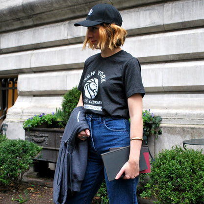 Woman wearing charcoal black crew neck t-shirt with the New York Public Library logo printed in the center.