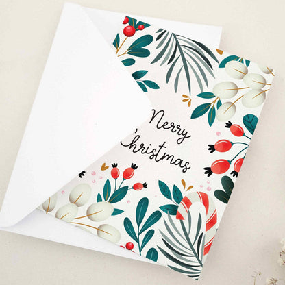 Card partially open, front decorated with colorful Christmas greenery, berries, and candy-cane details around “Merry Christmas” text — XOXOKristen.